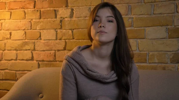 Closeup portrait of young attractive caucasian female being thoughtful and looking straight at camera in a cozy apartment indoors Stock Photo