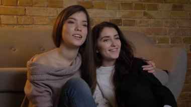 Portre portre sarılma ve heyecan içinde kapalı rahat bir daire ile Tv izlerken iki genç güzel kadın