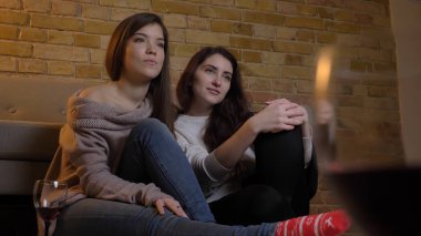 İki genç güzel kadın Tv ile şarap oturan rahat bir daire kapalı yerde ürpertici izlerken closeup portresi