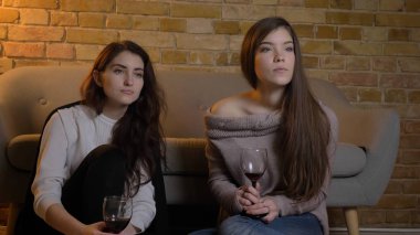 İki genç güzel kadın bir film Tv ürpertici laidback rahat bir daire kapalı yerde oturan şarap ile izlerken closeup portresi