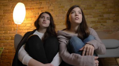 İki genç güzel kadın kapalı rahat bir daire içinde bir Tv programı izlerken portresi tabandan portre