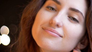 Closeup çekim gülümseyen ve bokeh arka plan ile kameraya bakarak genç çekici beyaz kadın yüz