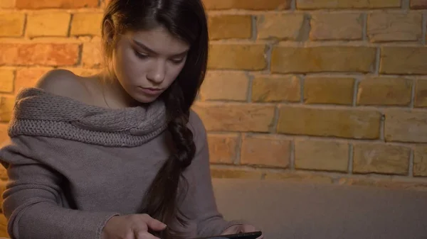 Nahaufnahme Porträt einer jungen attraktiven kaukasischen Frau, die auf dem Tablet tippt, während sie drinnen auf dem Sofa sitzt — Stockfoto
