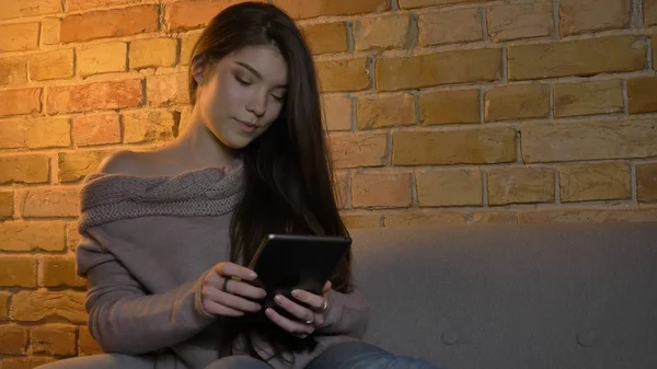 Nahaufnahme Porträt einer jungen attraktiven kaukasischen Frau, die auf dem Tablet SMS schreibt, während sie in einer gemütlichen Wohnung auf der Couch sitzt — Stockfoto