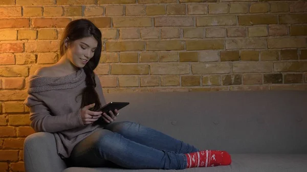 Nahaufnahme Porträt einer jungen attraktiven kaukasischen Frau, die das Tablet benutzt, während sie sich entspannt auf der Couch ausruht und drinnen zu Hause glücklich lächelt — Stockfoto