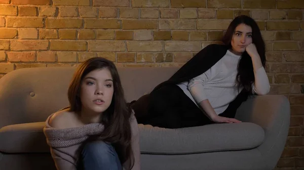 Retrato de close-up de duas jovens meninas bonitas assistindo TV com expressão facial fascinada enquanto descansa em um aconchegante apartamento dentro de casa — Fotografia de Stock