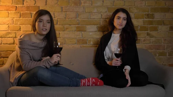Detailní portrét dvou mladých hezkých dívek, sledování televize a chlazení s vínem při odpočinku v útulném bytě uvnitř — Stock fotografie