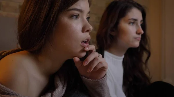 Closeup retrato de duas jovens mulheres bonitas assistindo TV com emoção em um aconchegante apartamento dentro de casa — Fotografia de Stock