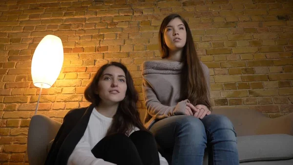 Närbild bottom-up-porträtt av två unga vackra kvinnor tittar på en film Tv i en mysig lägenhet inomhus — Stockfoto