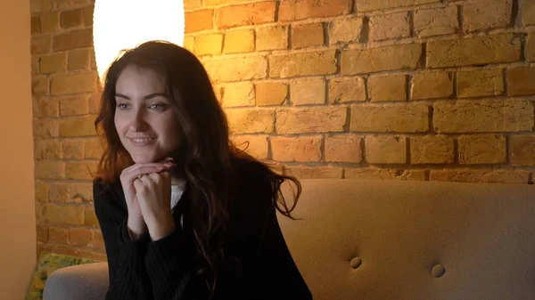 Closeup heyecan ve hayranlık rahat bir daire içinde kapalı kanepede otururken gülümseyen genç oldukça beyaz kadın Tv izlerken ateş