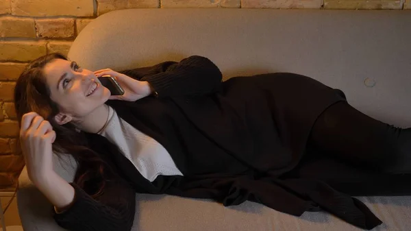Close-up tiro de jovem muito caucasiano morena fêmea deitado no sofá e chamando o telefone dentro de casa em um apartamento acolhedor — Fotografia de Stock