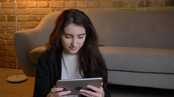 Closeup portret van de jonge vrij Kaukasische vrouwelijke browsen op de tablet in een gezellig huis binnenshuis — Stockfoto