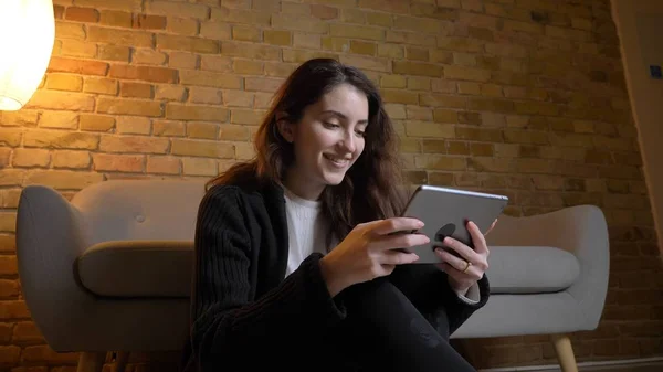 Nahaufnahme Porträt einer jungen hübschen kaukasischen Frau, die mit lächelndem Gesichtsausdruck auf dem Tablet in einem gemütlichen Haus drinnen SMS schreibt — Stockfoto