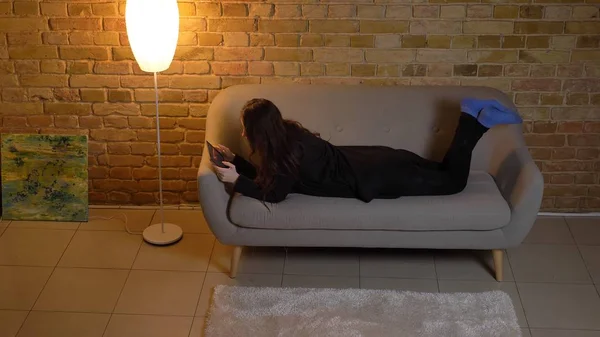 Κινηματογράφηση σε πρώτο πλάνο το top view πορτρέτο του νέους αρκετά καυκάσιος γυναίκα περιήγηση στο tablet ξαπλωμένοι στον καναπέ σε ένα άνετο σπίτι σε εσωτερικούς χώρους — Φωτογραφία Αρχείου