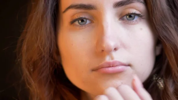 Close-up tiro de jovem rosto feminino caucasiano atraente sendo pensativo olhando para a câmera com fundo bokeh — Fotografia de Stock