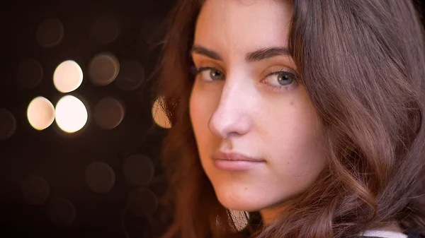 Closeup side view shoot of young attractive caucasian female face turning and looking at camera with bokeh lights on the background — Stock Photo, Image