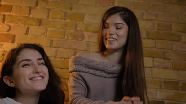 Closeup bottom up portrait of two young pretty women watching TV laughing happily in a cozy apartment indoors Stock Picture