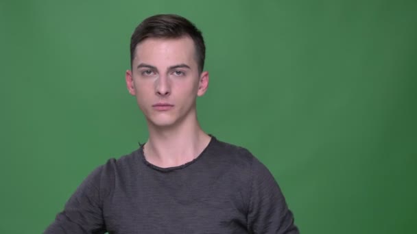 Genç yakışıklı beyaz erkek garip yapma portre çekimleri dans hamle yeşil izole arka plan ile doğrudan kameraya bakıyor — Stok video
