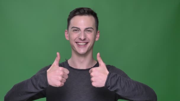 Closeup shoot of young handsome caucasian maleshowing thumbs up looking straight at camera with background isolated on green — Stock Video