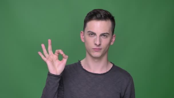 Closeup shoot of young handsome caucasian malegesturing ok handsign looking straight at camera with background isolated on green — Stock Video