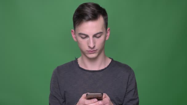 Close-up opnamen van jonge knappe Kaukasische man de telefoon gebruikt met geïsoleerd op groene achtergrond — Stockvideo