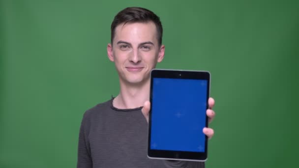 Nahaufnahme Shooting von jungen schönen kaukasischen Mann mit dem Tablet mit blauem Chroma-Bildschirm mit Hintergrund isoliert auf grün — Stockvideo