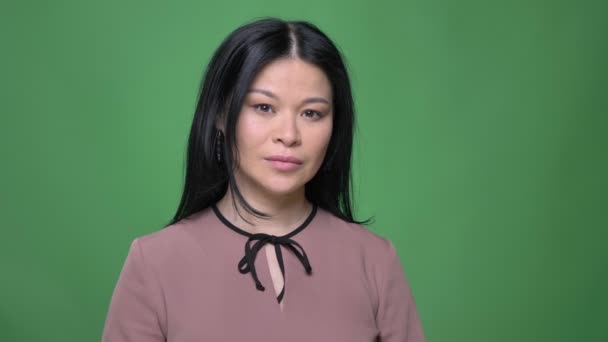 Съемки крупным планом молодой привлекательной азиатской женщины с черными волосами, смотрящей прямо в камеру с изолированным на зеленом фоне — стоковое видео