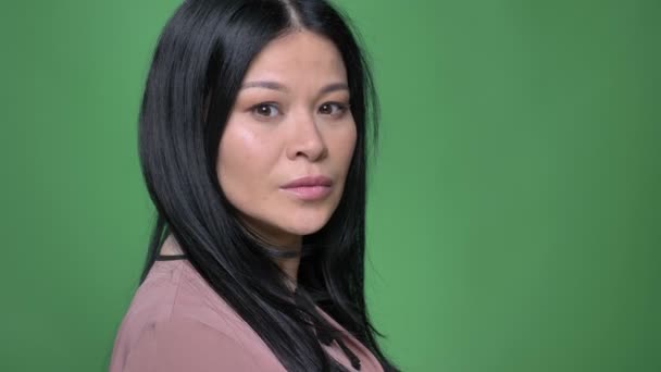 Съемки крупным планом молодых привлекательных азиатских женщин, поворачивающихся и смотрящих прямо в камеру с изолированным на зеленом фоне — стоковое видео