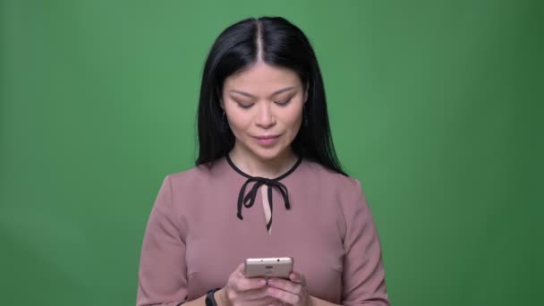 Closeup natáčení mladé atraktivní asijské ženy s černými vlasy pomocí telefonu s pozadím izolované na zelené — Stock video