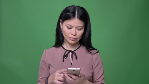 Zbliżenie strzelać z młodych atrakcyjnych azjatyckich kobiet z czarnymi włosami, surfing mediów społecznych telefon i reakcji z tła na zielonym tle — Wideo stockowe