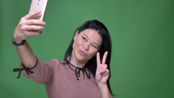 Närbild-shoot av unga attraktiva asiatisk kvinna med svart hår att ta selfies på den telefonen och poserar framför kameran med bakgrund som isolerade på gröna — Stockvideo