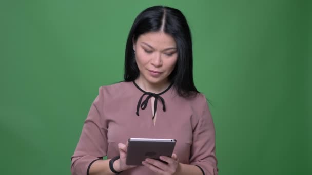 Vértes lő a fiatal vonzó ázsiai nő-val fekete haj textil a Tablet elszigetelt zöld háttérrel — Stock videók