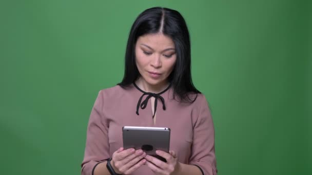 Vértes lő a fiatal vonzó ázsiai nő-val fekete haj textil a tabletta és látszó-on fényképezőgép-val döbbent arckifejezés elszigetelt zöld háttérrel — Stock videók
