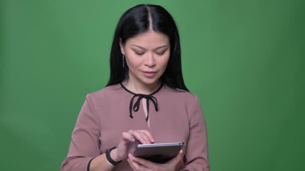 Close-up tiro de jovem atraente asiático fêmea com preto cabelo usando o tablet e mostrando azul tela para câmera — Vídeo de Stock