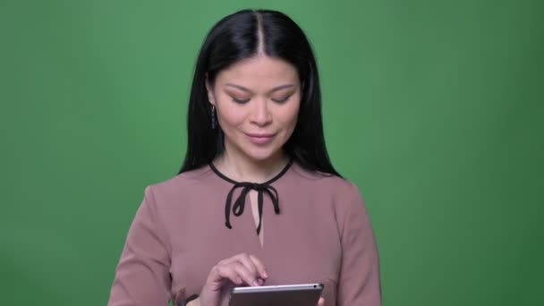 Nahaufnahme einer jungen attraktiven asiatischen Frau mit schwarzen Haaren, die das Tablet benutzt und der Kamera den blauen Chroma-Bildschirm zeigt — Stockvideo