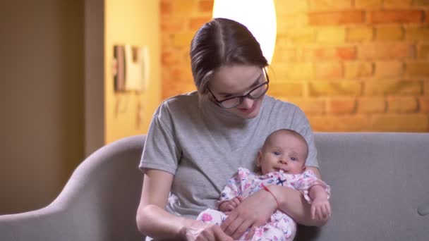 Retrato de mãe abraçando sua filha recém-nascida bonito sentado no sofá na sala de estar . — Vídeo de Stock
