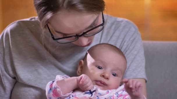 Närbild porträtt av mor kysser hennes söta och vackra nyfödda dotter i vardagsrummet. — Stockvideo