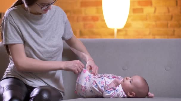 Porträt einer Mutter, die ihrer süßen neugeborenen Tochter Windeln wechselt, die auf dem Sofa im Wohnzimmer liegt. — Stockvideo