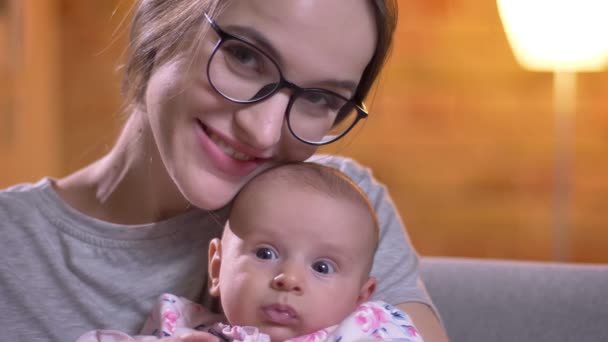 Крупним планом портрет матері обіймає зі своєю милою новонародженою дочкою і дивиться посміхаючись у камеру у вітальні . — стокове відео