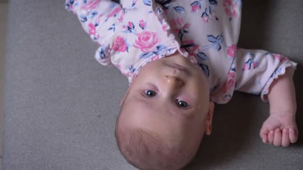 Upside down close-up top shot of pretty newborn girl lying on sofa and watching into camera attentively. — Stock Video