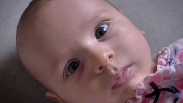 Close-up portrait of pretty newborn girl lying on sofa and watching into camera intently. — Stock Video