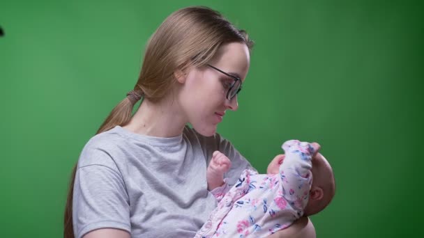 Крупный план портрет красивой матери, держащей и целующей свою милую и красивую новорожденную дочь на зеленом фоне . — стоковое видео