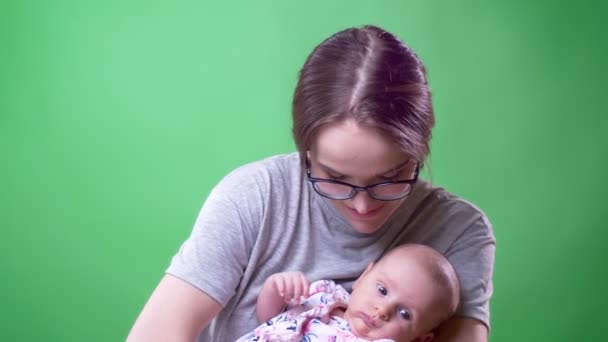 Nahaufnahme Porträt der hübschen Mutter posiert und hält ihre süße und hübsche neugeborene Tochter auf grünem Hintergrund. — Stockvideo