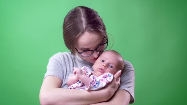 Närbild porträtt av vackra mor poserar hennes söta nyfödda dotter som gäspar prettily på grön bakgrund. — Stockvideo