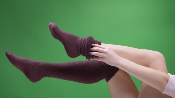 Крупный план женских подростковых ног в милых красно-белых носках, игриво движущихся на заднем плане, изолированных на зеленом. Девушка одевает свой коленный носок — стоковое видео