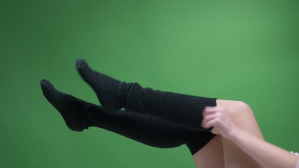 Nahaufnahme von weiblichen Teenagerbeinen in niedlichen schwarzen Stricksocken, die sich spielerisch mit einem auf Grün isolierten Hintergrund bewegen. Mädchen zieht ihre Kniestrümpfe an — Stockvideo