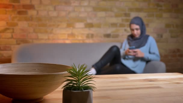 Nahaufnahme einer jungen attraktiven muslimischen Frau im Hijab mit dem Handy, während sie sich zu Hause entspannt auf der Couch ausruht — Stockvideo