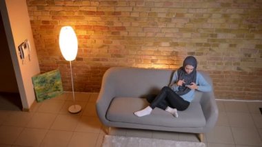 Telefonda genç çekici Müslüman kadın mesajlaşma Shoot çekim rahat evde kanepede kapalı rahat olmak