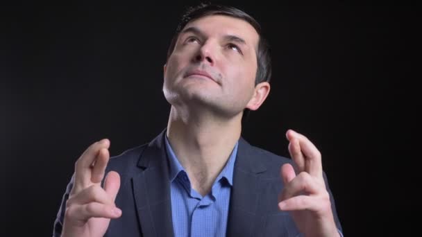 Cloesup shoot van volwassen hoopvolle Kaukasische man met zijn vingers gekruist en bedelen kijken recht op camera met achtergrond geïsoleerd op zwart — Stockvideo