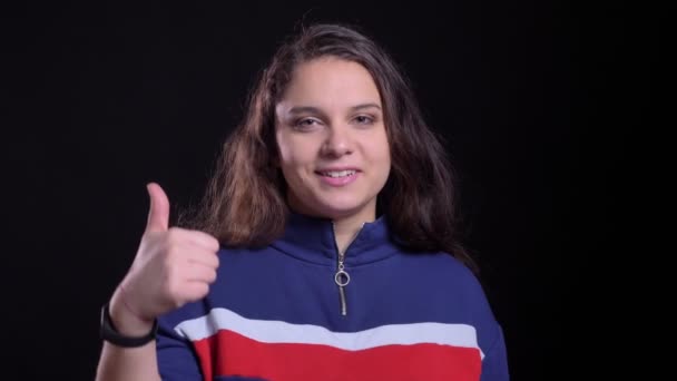 Close-up portret van volwassen aantrekkelijke Kaukasische vrouw toont een duim omhoog en glimlachend vrolijk voor de camera met achtergrond geïsoleerd op zwart — Stockvideo